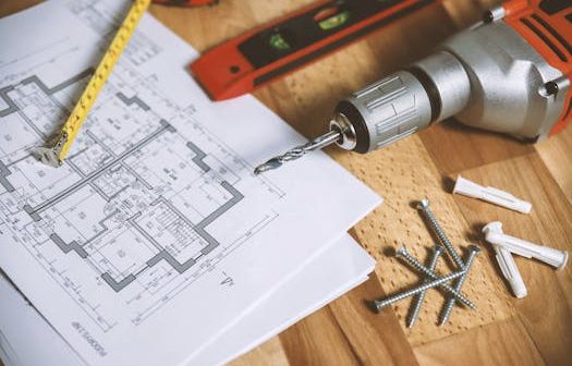 Close-up of construction blueprint with tools like drill and screws on a wooden table.